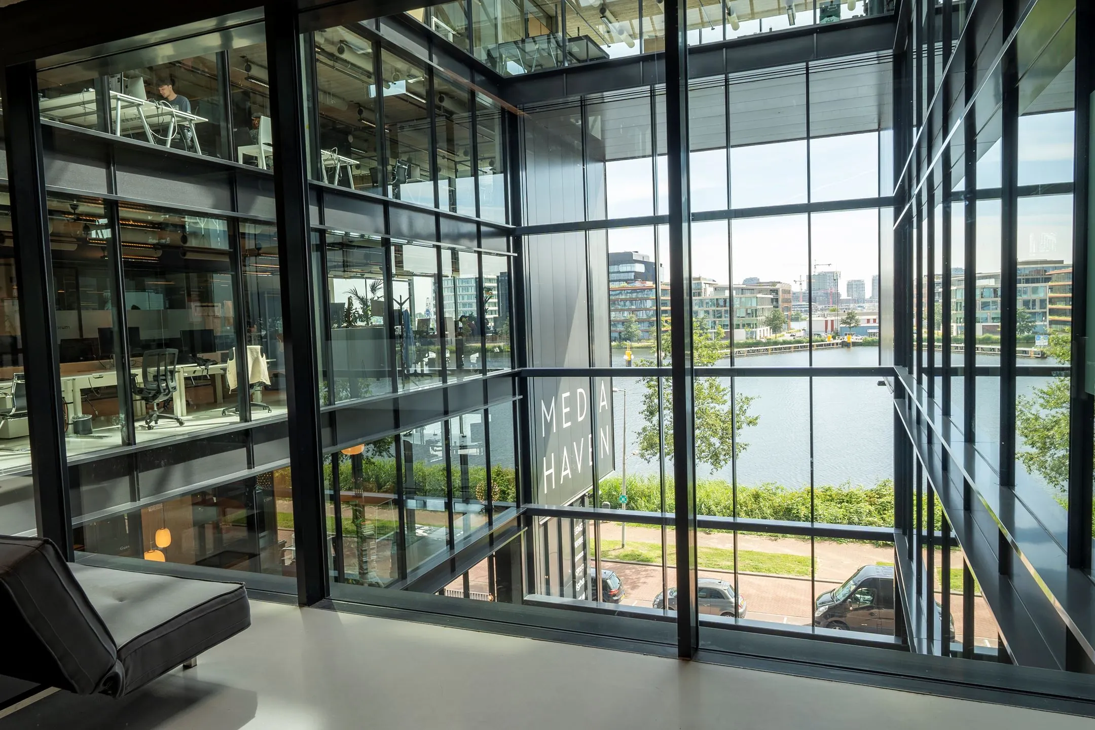 Zicht op moderne kantoorverdiepingen en het water vanaf binnen in het glazen gebouw aan de Moermanskkade 109, met ‘Mediahaven’ zichtbaar op de gevel.
