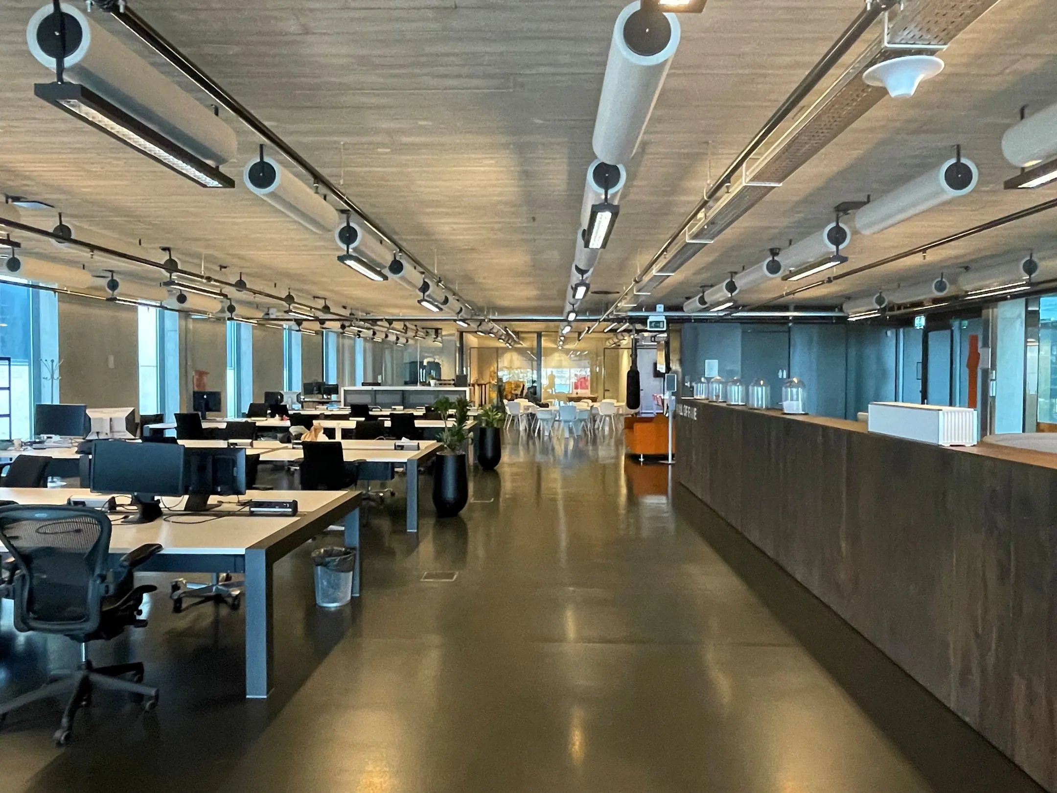 Moderne en ruime kantooretage aan de Moermanskkade 109 met open werkplekken, een betonnen plafond en een lange balie.