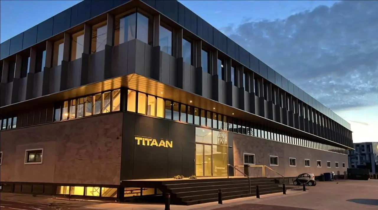 Modern kantoorgebouw TITAAN met strakke architectuur en verlichting in de avondschemering.