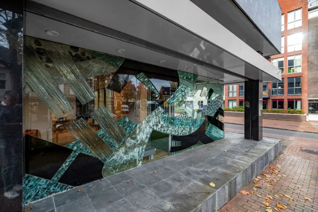 Glazen kunstwerk met abstracte vormen in de etalage van een gebouw aan de ’s-Gravelandseweg 9.