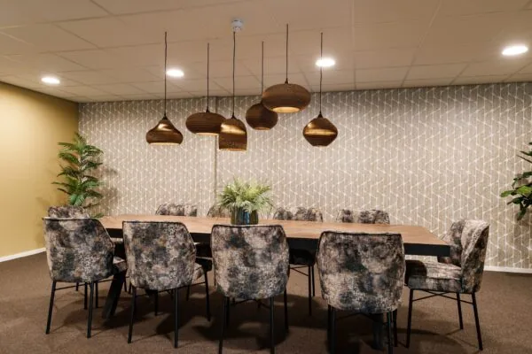 Vergaderruimte aan de ’s-Gravelandseweg 9 met grote houten tafel, gestoffeerde stoelen en hanglampen in warme tinten.