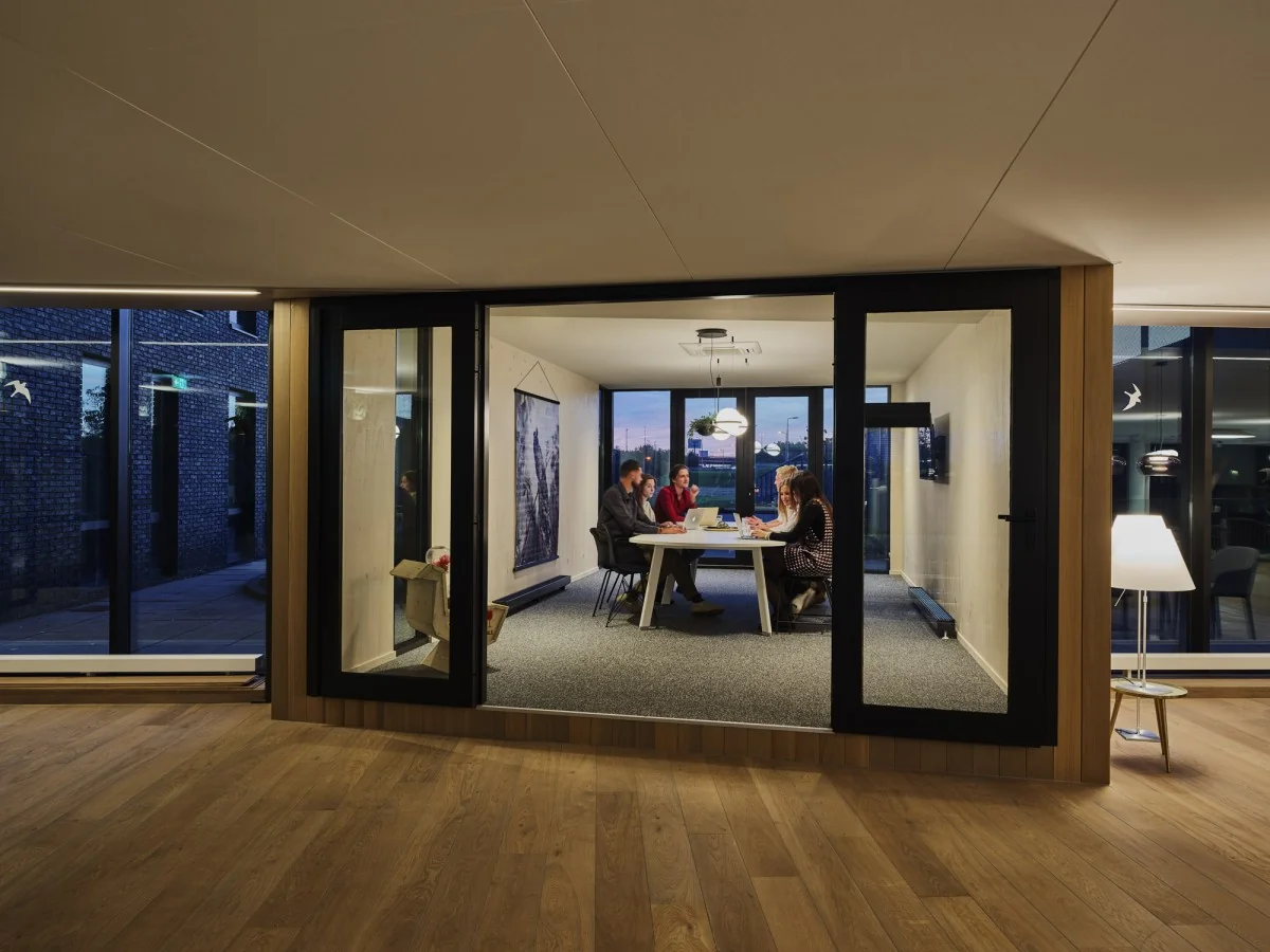 Vergaderruimte met glazen wanden aan de Van Deventerlaan 31-51, waarin vijf mensen rond een tafel overleggen.