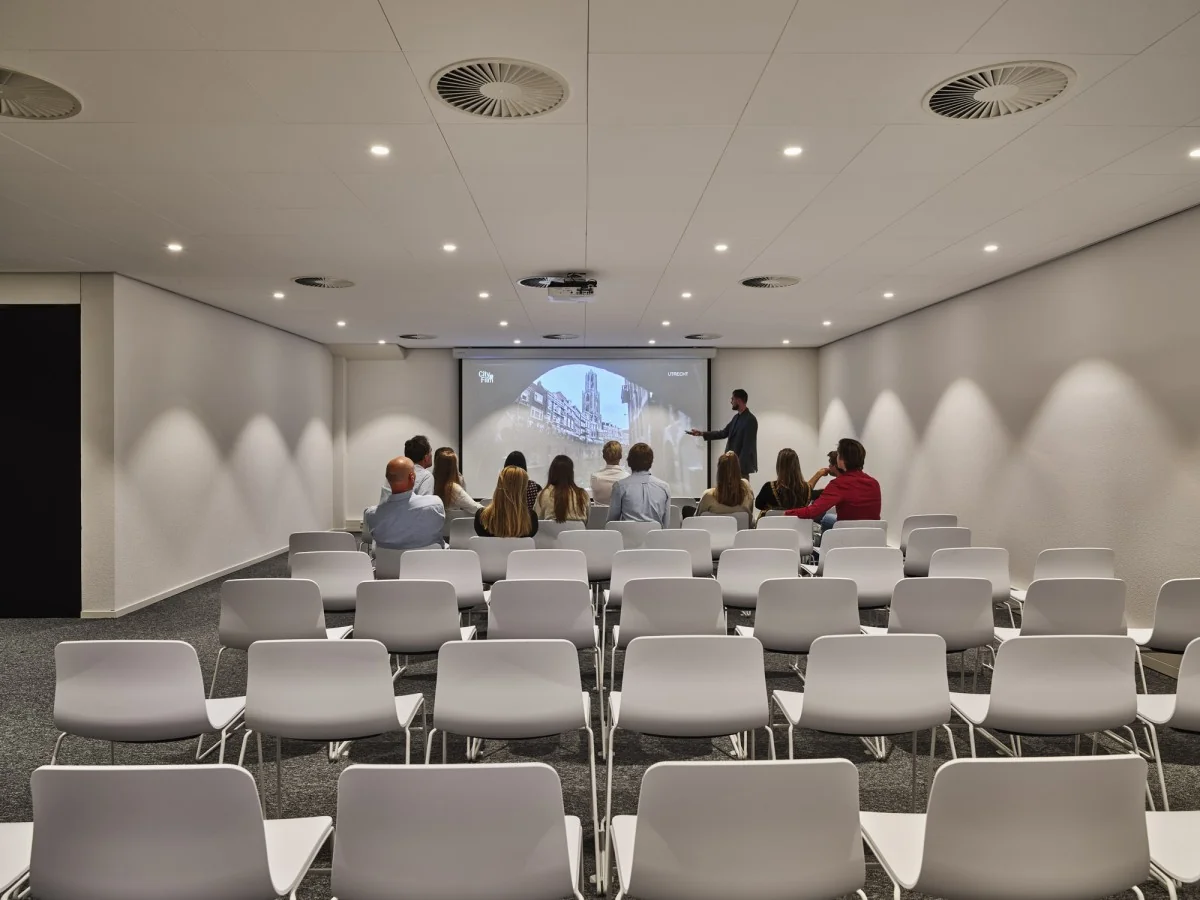 Presentatie in een moderne vergaderruimte aan de Van Deventerlaan 31-51 met enkele aanwezigen en een spreker voor een projectiescherm.