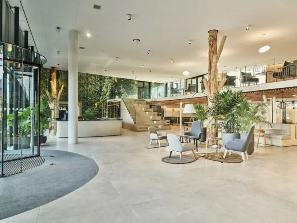 Moderne, ruim opgezette kantoorlobby aan de Van Deventerlaan 31-51 met houten accenten, zitgedeeltes en veel groen.