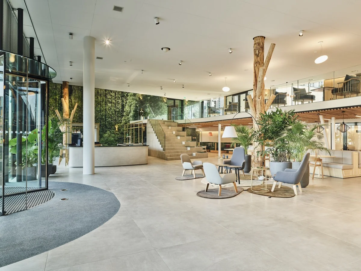 Moderne, ruim opgezette kantoorlobby aan de Van Deventerlaan 31-51 met houten accenten, zitgedeeltes en veel groen.