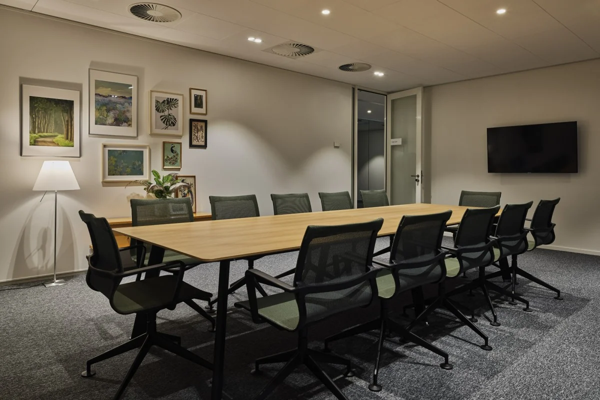 Moderne vergaderruimte aan de Van Deventerlaan 31-51 met lange tafel, zwarte stoelen, kunst aan de muur en een flatscreen.