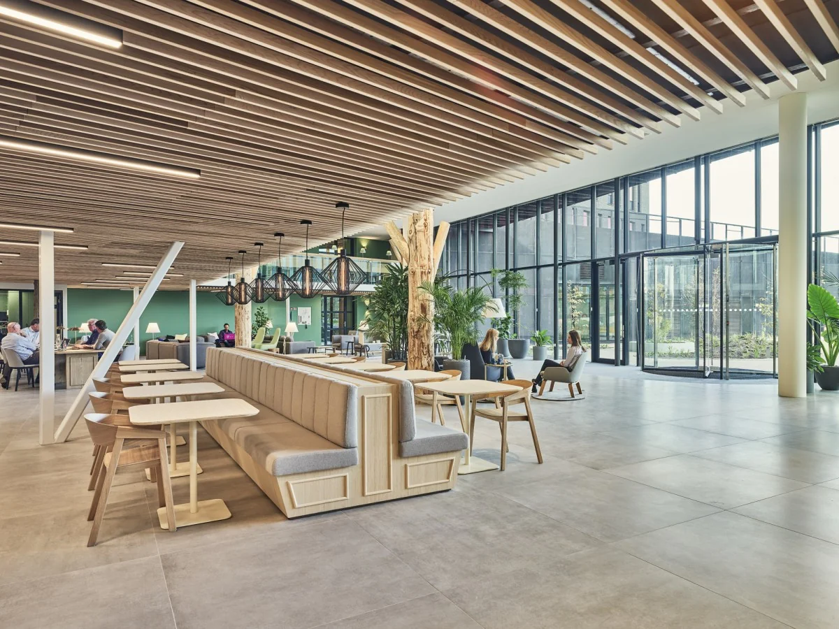 Moderne en ruim opgezette lobby van kantoorgebouw Van Deventerlaan 31-51 met zithoeken, houten plafondaccenten en grote glazen gevel.
