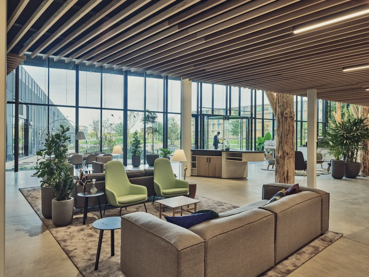 Moderne, open kantoorlobby aan de Van Deventerlaan 31-51 met comfortabele zitplekken, veel planten en grote ramen met uitzicht op buiten.