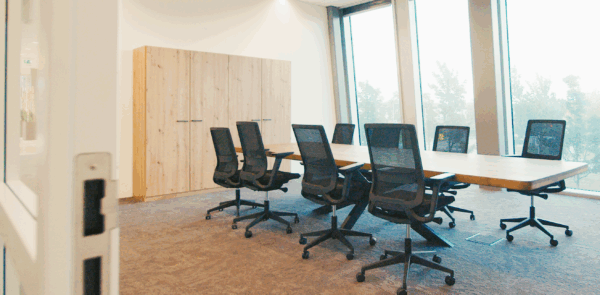 Moderne vergaderkamer met grote houten tafel, zwarte bureaustoelen en hoge ramen met uitzicht.
