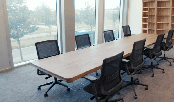 Moderne vergaderkamer met een lange houten tafel, zwarte bureaustoelen en grote ramen met uitzicht op de straat.