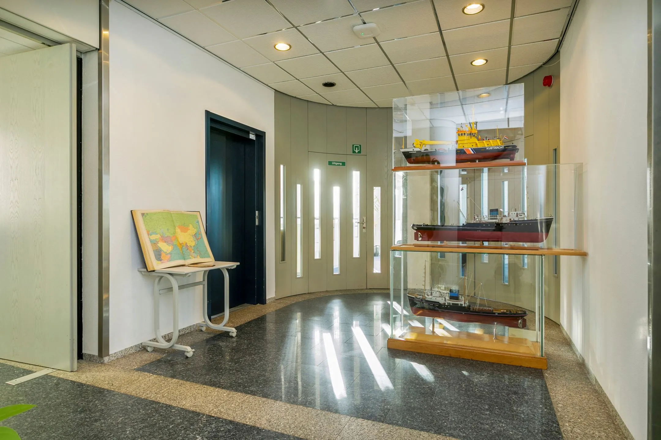 Hal met vitrinekast met schaalmodellen van schepen en een wereldkaart op een lessenaar in een gebouw in Maassluis.