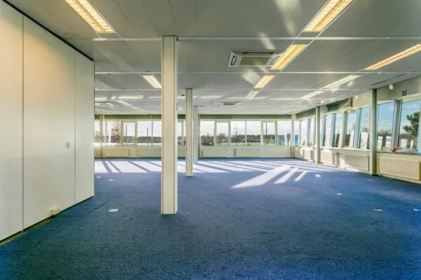 Licht en ruim kantoorpand in Maassluis met blauwe vloerbedekking en grote ramen rondom.