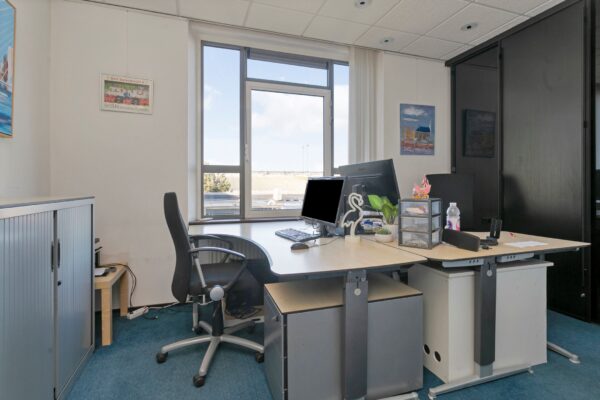 Modern kantoor met twee bureaus, computers en uitzicht op een zonnige buitenomgeving in Maassluis.