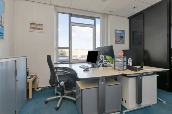 Modern kantoor met twee bureaus, computers en uitzicht op een zonnige buitenomgeving in Maassluis.