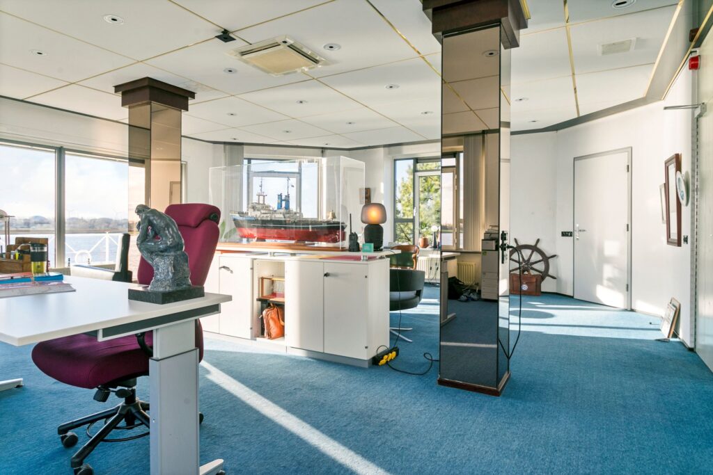Modern kantoor met maritieme decoratie, waaronder een groot modelschip en een houten scheepsstuurwiel, in Maassluis.