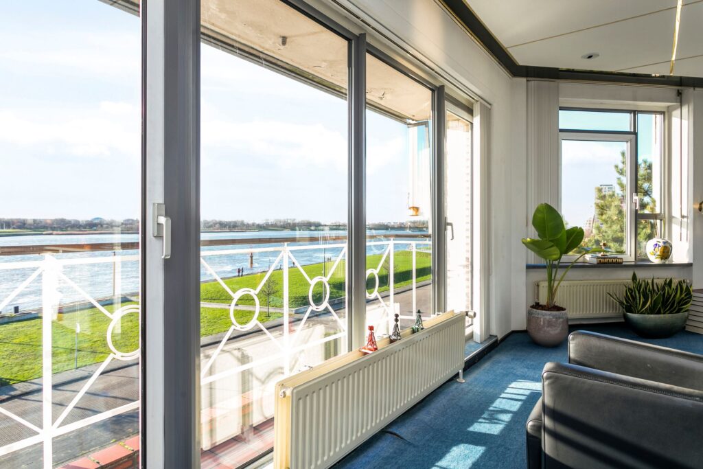 Woonkamer met grote ramen en uitzicht op het water en de groene kade in Maassluis.