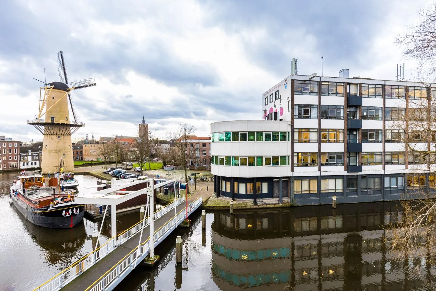 Uitzicht op de Noordvest in Schiedam met een molen, kantoorgebouw en aangemeerde schepen aan het water.