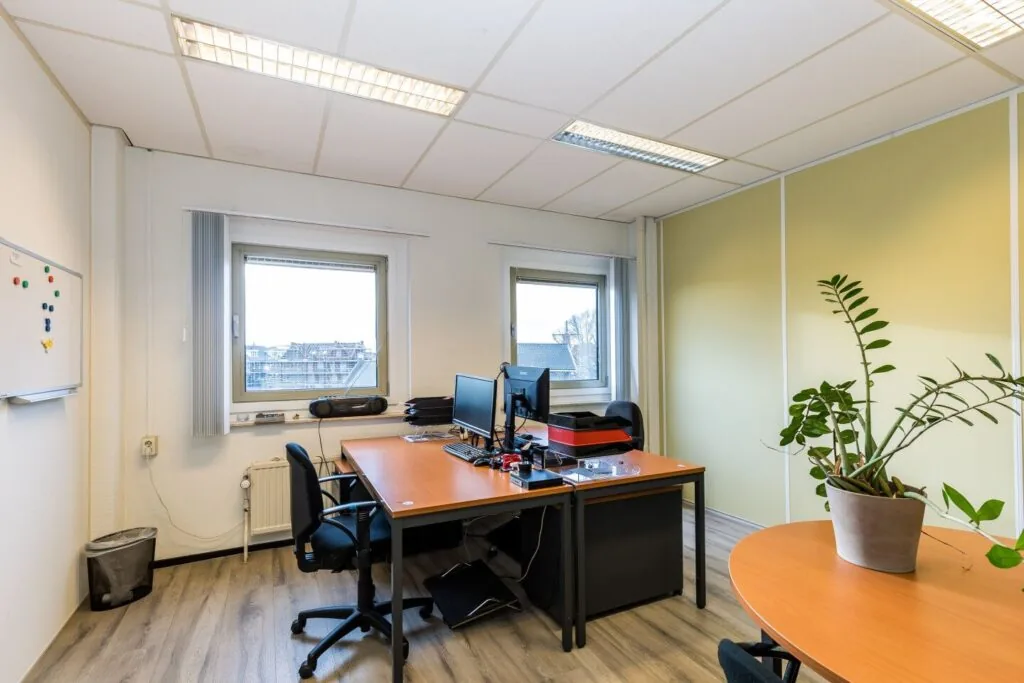 Klein, licht kantoor in het gebouw aan de Noordvest in Schiedam met twee bureaus, computers en een grote kamerplant.