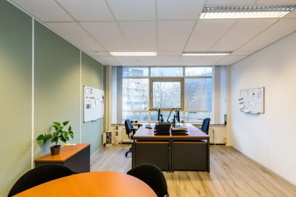Moderne kantoorruimte aan de Noordvest in Schiedam met bureaus, stoelen, computers en een groot raam met uitzicht op flatgebouwen.