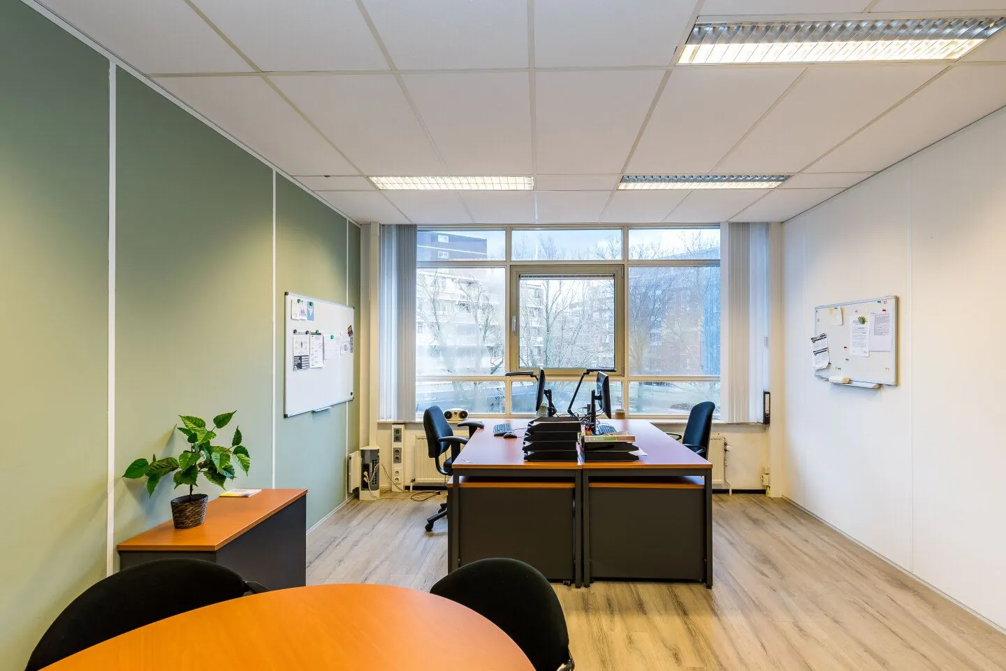 Moderne kantoorruimte aan de Noordvest in Schiedam met bureaus, stoelen, computers en een groot raam met uitzicht op flatgebouwen.