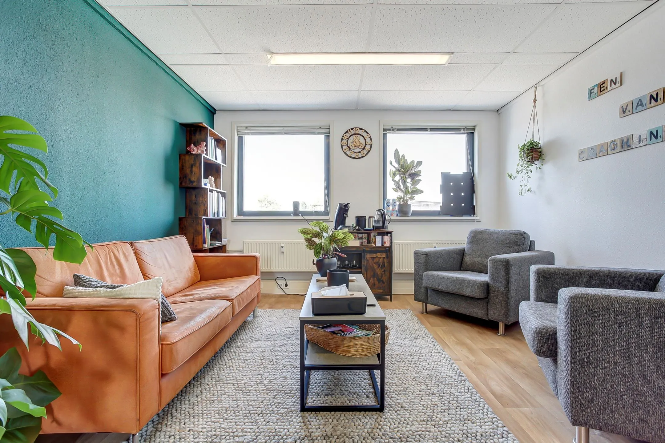 Modern ingerichte wacht- of gespreksruimte aan de Groenestraat 294 met een oranje bank, grijze fauteuils en veel natuurlijk licht.