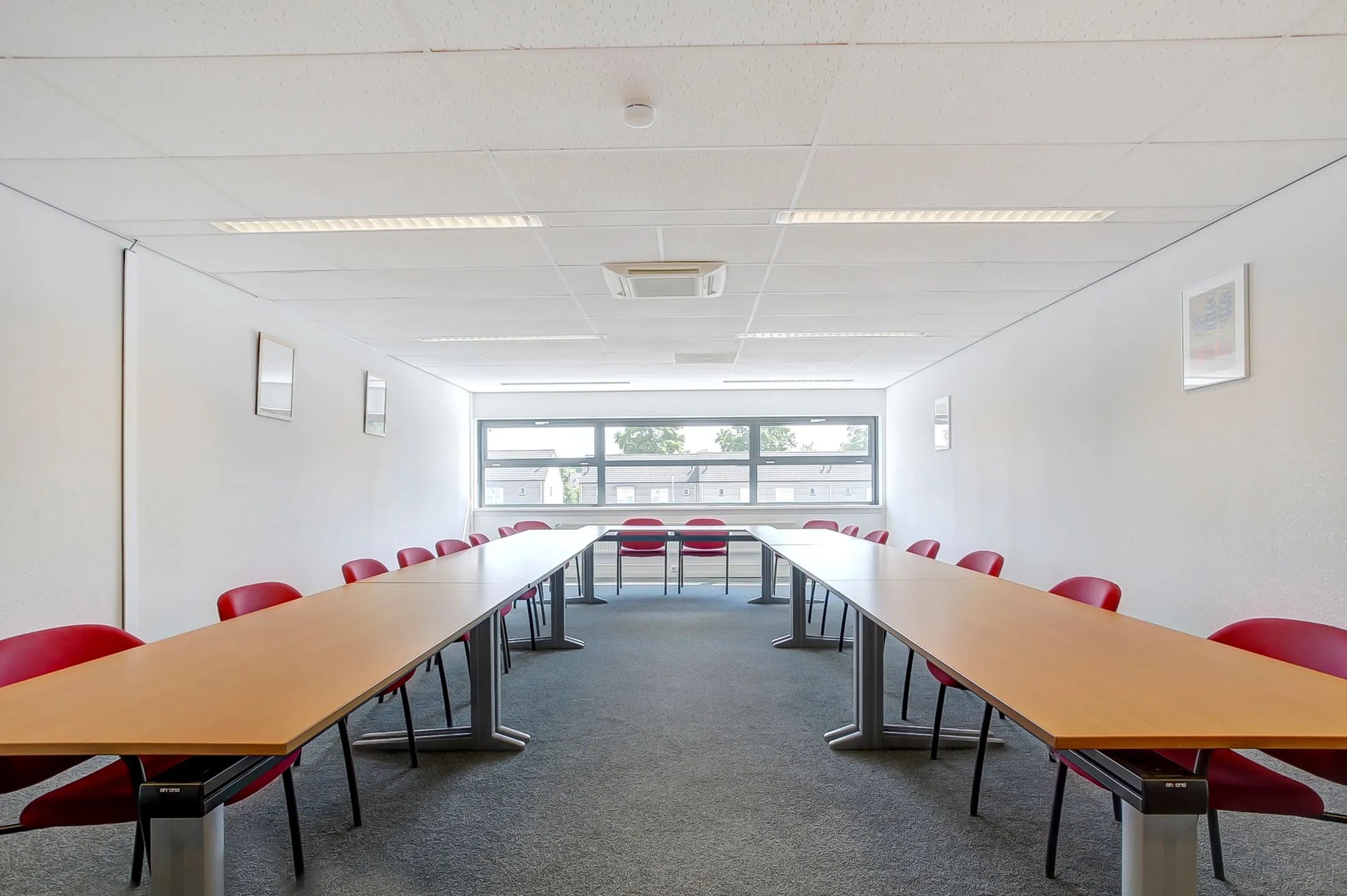 Vergaderruimte aan de Groenestraat 294 met U-vormige opstelling van tafels en rode stoelen.