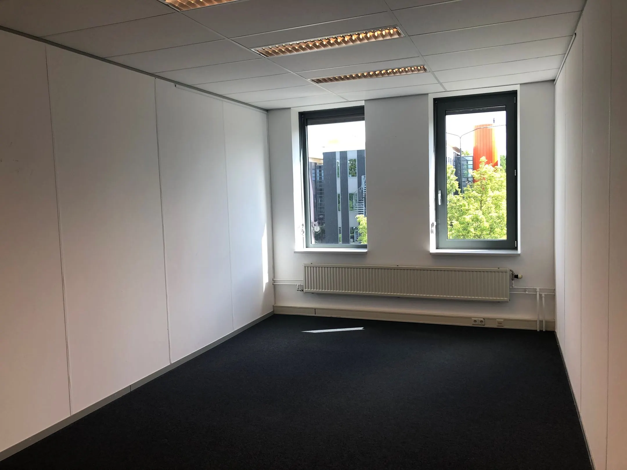 Leeg, licht kantoorruimte in Kerkenbos 1033-1037 met twee ramen en donkere vloerbedekking.