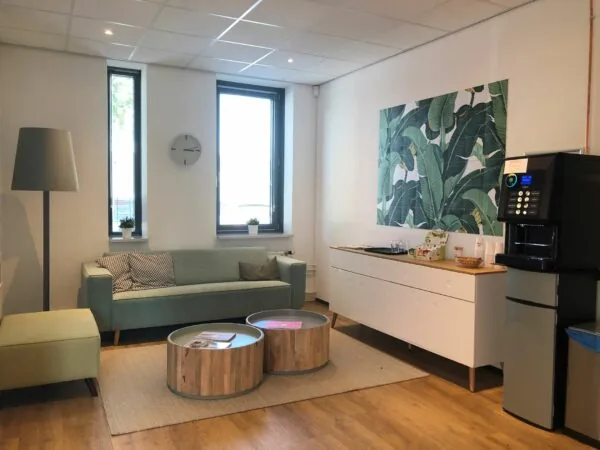 Gezellige wachtruimte in Kerkenbos 1033-1037 met zitbank, koffietafel, koffieautomaat en groene wanddecoratie.