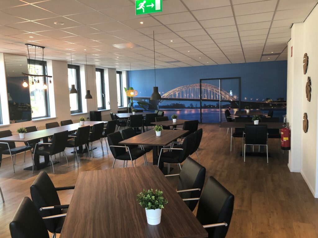 Moderne, ruim opgezette vergaderruimte in Kerkenbos 1033-1037 met houten tafels, zwarte stoelen en een muurprint van de Waalbrug in Nijmegen.