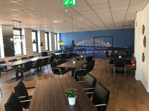 Moderne, ruim opgezette vergaderruimte in Kerkenbos 1033-1037 met houten tafels, zwarte stoelen en een muurprint van de Waalbrug in Nijmegen.