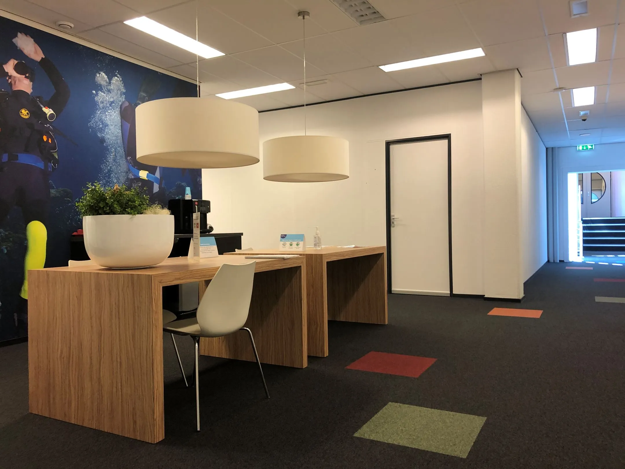 Moderne ontvangstruimte in het kantoorpand Kerkenbos 1033-1037 met houten balie, designstoelen en duikthema-muurschildering.