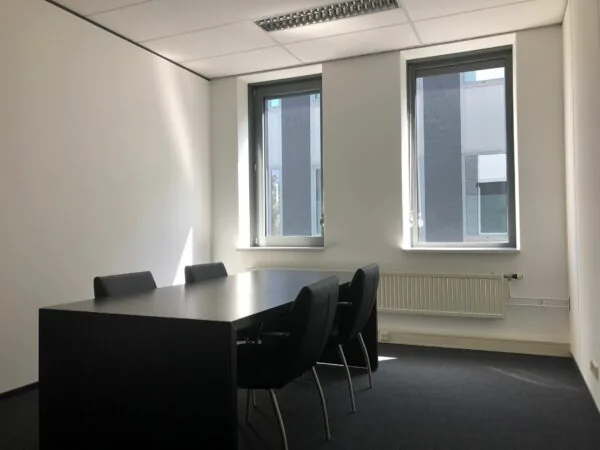 Kleine vergaderruimte in kantoorpand Kerkenbos 1033-1037 met tafel, zes stoelen en twee ramen.