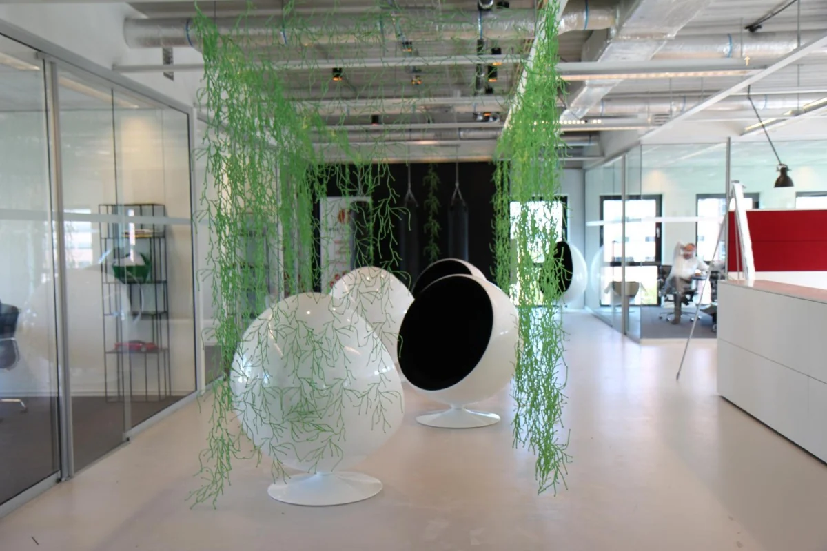 Moderne kantoorruimte aan het John M. Keynesplein in Amsterdam met futuristische zitstoelen en hangende groene decoratie.