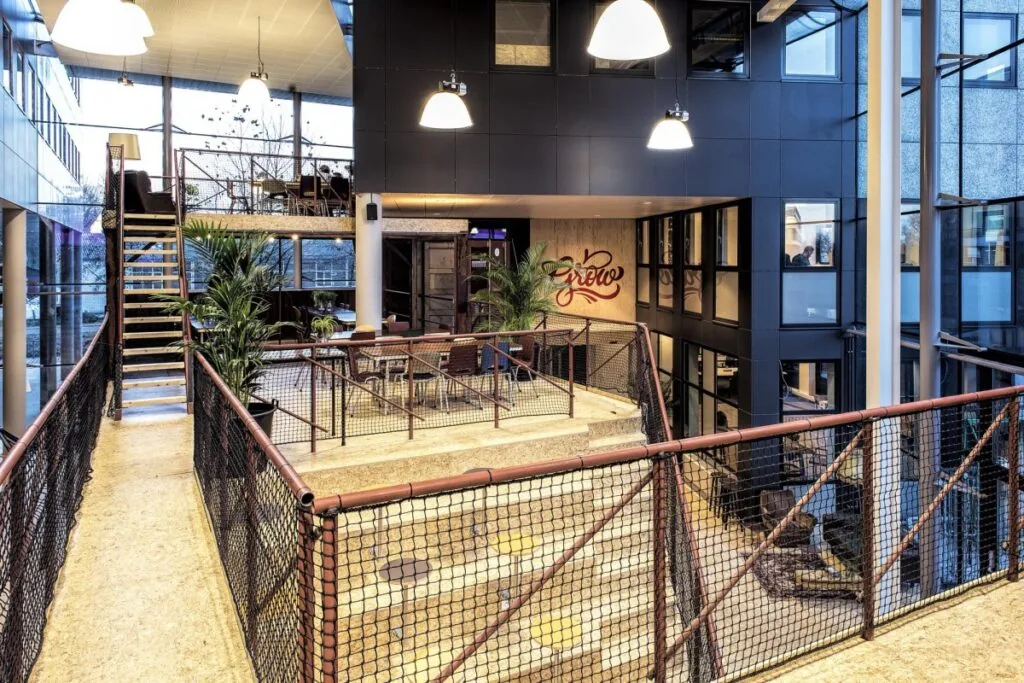 Moderne gemeenschappelijke ruimte in een kantoorgebouw aan het John M. Keynesplein in Amsterdam met zitplekken, planten en industriële inrichting.