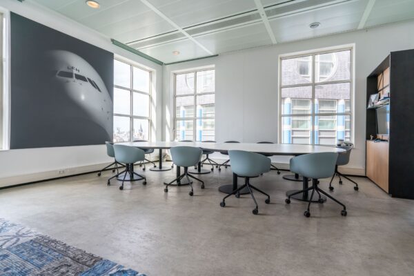 Moderne vergaderruimte in kantoorruimte aan de Turfmarkt 104 met ovale vergadertafel, lichtblauwe stoelen en groot raam.