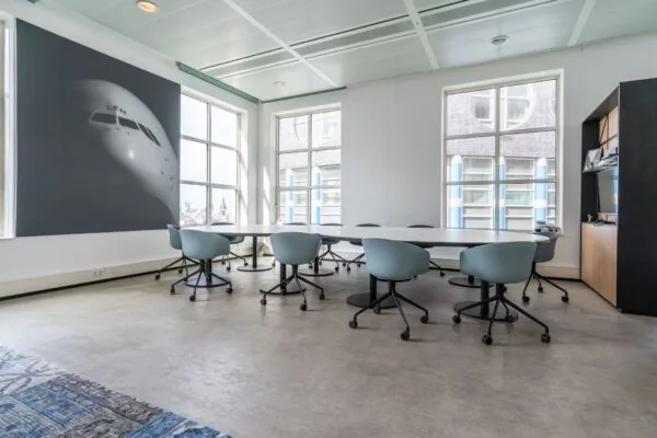 Moderne vergaderruimte in kantoorruimte aan de Turfmarkt 104 met ovale vergadertafel, lichtblauwe stoelen en groot raam.
