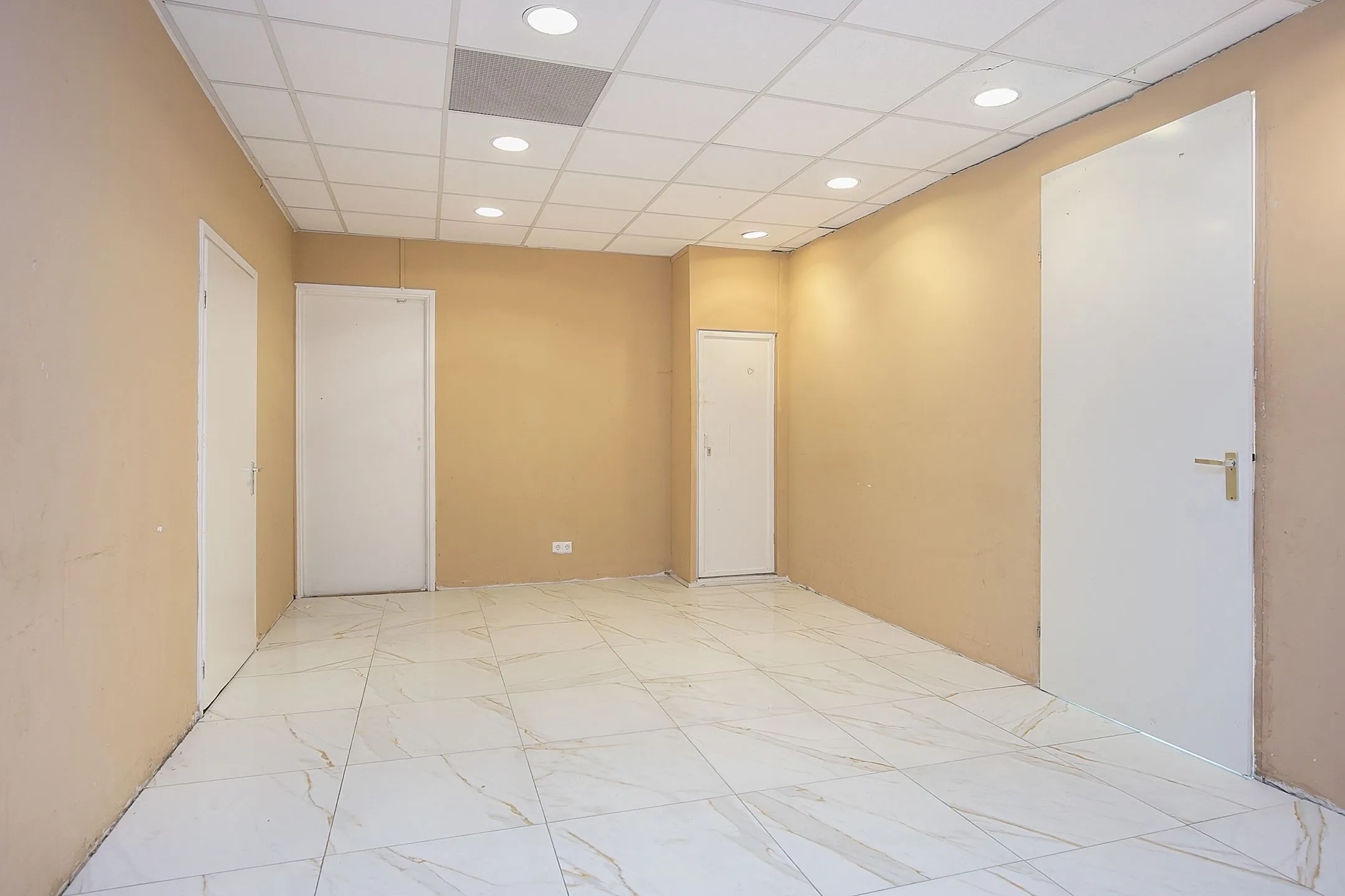 Lege kamer in Weena 113 met beige muren, witte deuren en glanzende marmeren vloer.