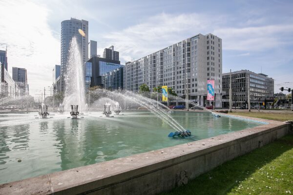 Fontein op het Weena in Rotterdam met hoog opspuitend water, omringd door moderne hoogbouw.