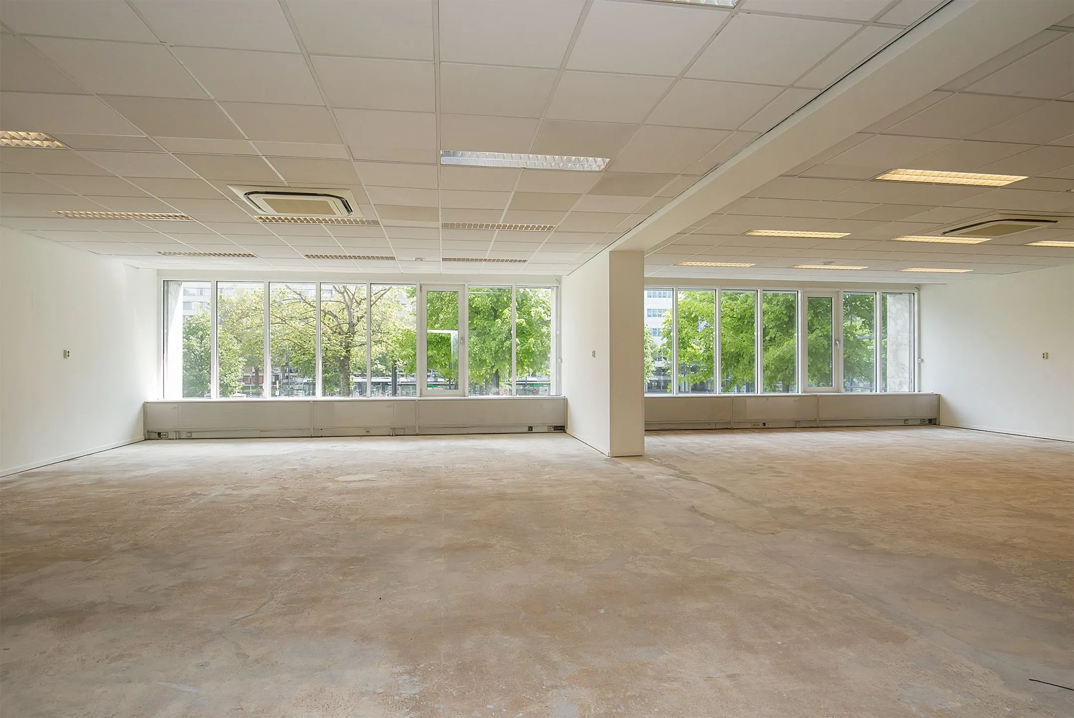 Leeg kantoorpand aan de Weena 75 met grote ramen en uitzicht op groene bomen.