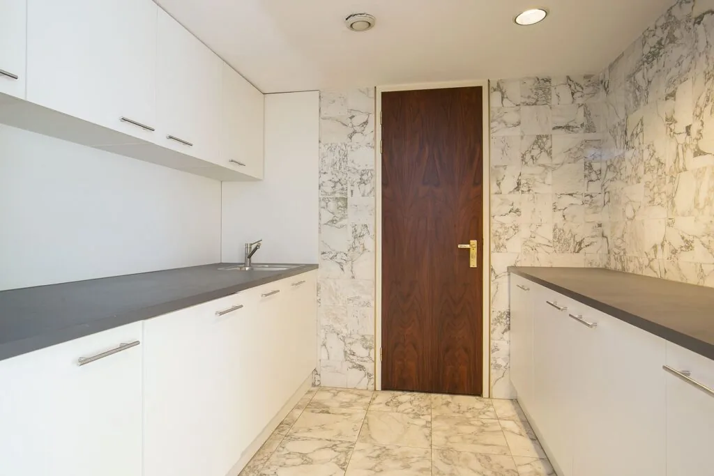 Moderne kitchenette met witte kasten, donker werkblad en marmeren vloer en wanden in Weena 75.