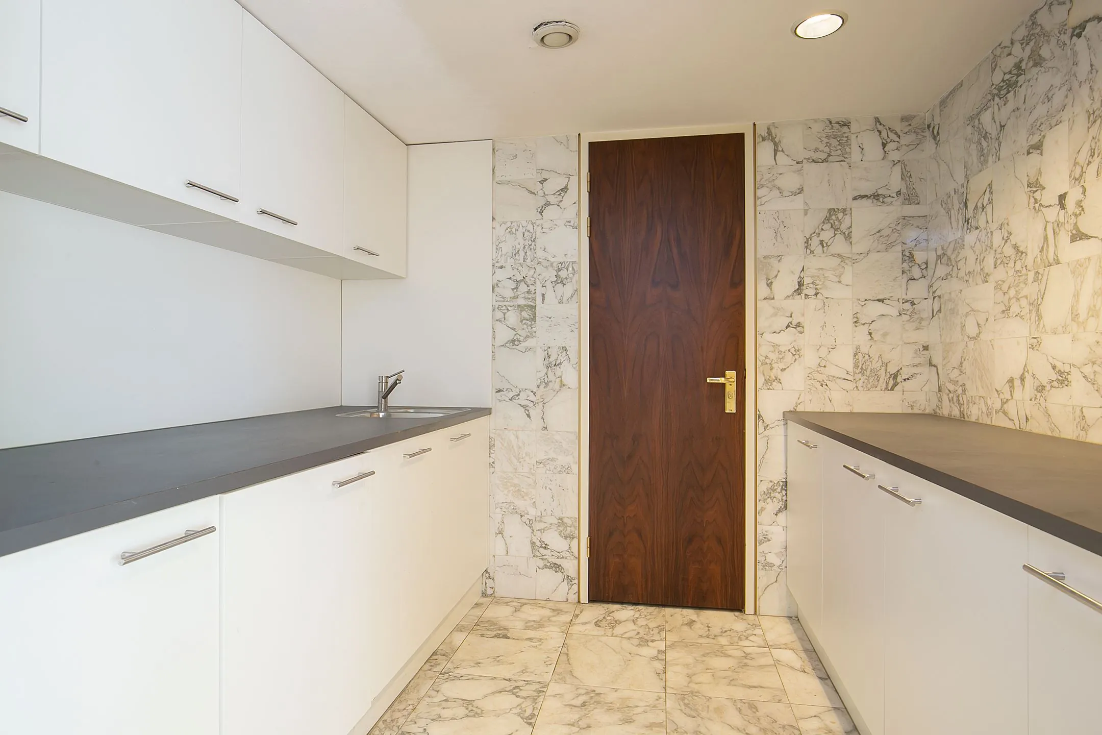 Moderne kitchenette met witte kasten, donker werkblad en marmeren vloer en wanden in Weena 75.