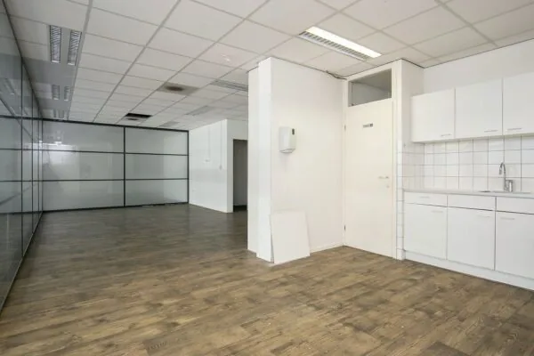 Leeg kantoorinterieur in Weena 81 met glazen scheidingswand, systeemplafond en pantry met witte keukenkastjes.