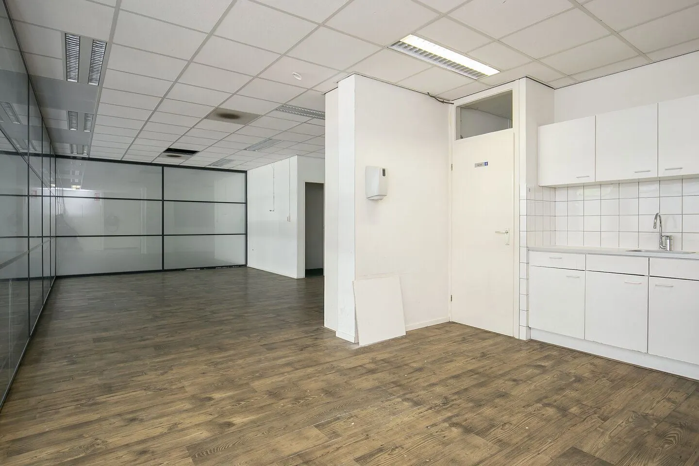 Leeg kantoorinterieur in Weena 81 met glazen scheidingswand, systeemplafond en pantry met witte keukenkastjes.