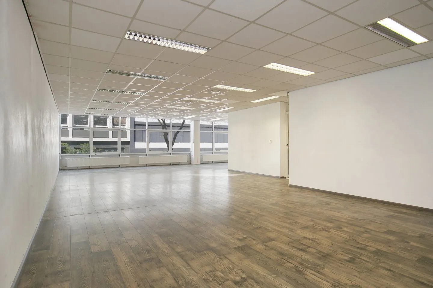 Lege kantoorruimte in Weena 81 met systeemplafond, grote ramen en houtlook vloer.