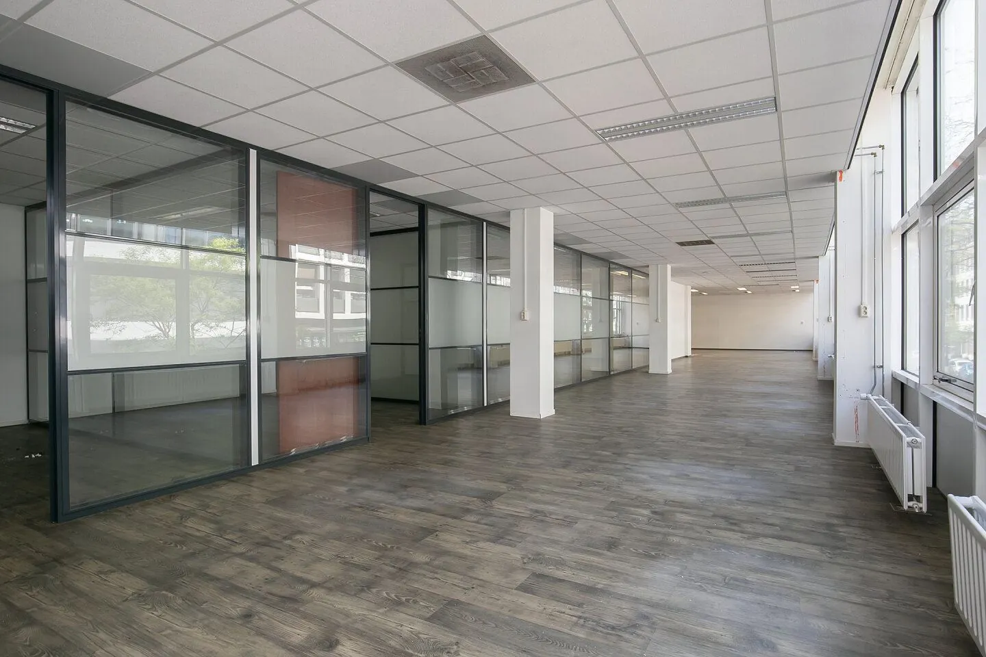 Een ruime, leegstaande kantoorruimte in Weena 81 met glazen scheidingswanden en grote ramen.